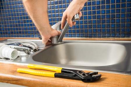 Image of a plumber working on plumbing of a kitchen sink and using a wrench on a tap..